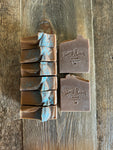 Image shows a group of brown soaps with blue glitter on top.