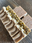 Image shows a group of tan colored soaps with little specks in them and chamomile on top.