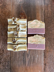 Image shows a group of purple and green and white soaps with botanicals on top