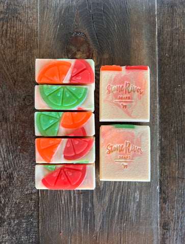 Image shows a group of white soaps with colorful swirls and topped with citrus soap slices. 