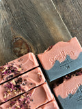 Image shows a group of black and pink soaps with rose petals and black sea salts on top