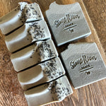 Image shows a group of bluish grey soaps topped with black sea salt.