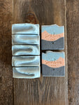 Image shows a group of black, orange, and blue soaps with loofah shreds inside. 