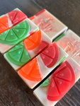Image shows a group of white soaps with colorful swirls and topped with citrus soap slices.
