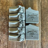 Image shows a group of bluish grey soaps topped with black sea salt.