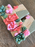 Image shows a group of green and tan soaps topped with colorful succulent soaps