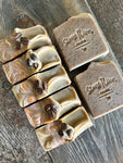 Image shows a group of brown soaps filled with coffee grounds and topped with mica and coffee beans.