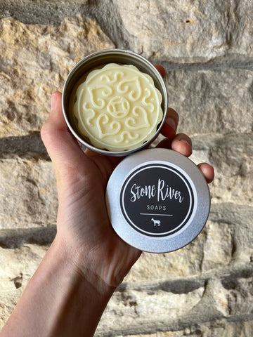 Image shows someone holding a solid lotion bar in a tin.